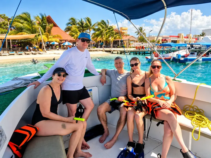 Guests and crew seated aboard the same boat under its dark blue canopy.
