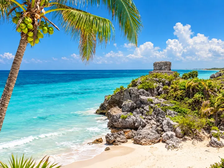 Tulum beach with foreground palm and archaeological structure in the distance.